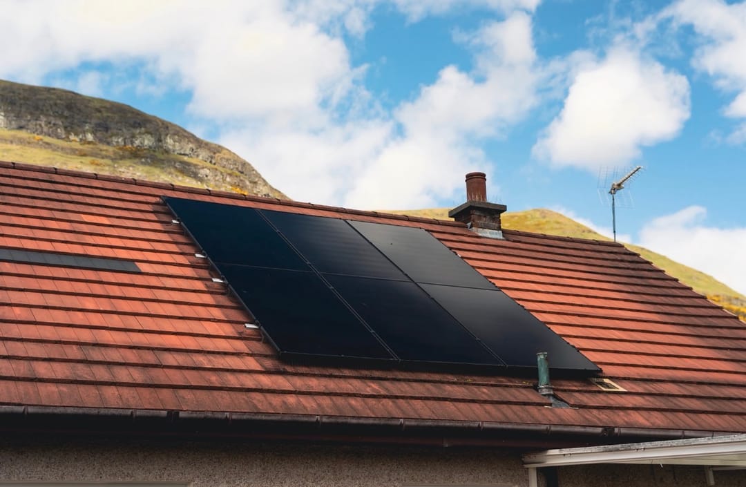 Black solar panels on a red tiled roof below the Ochil hills