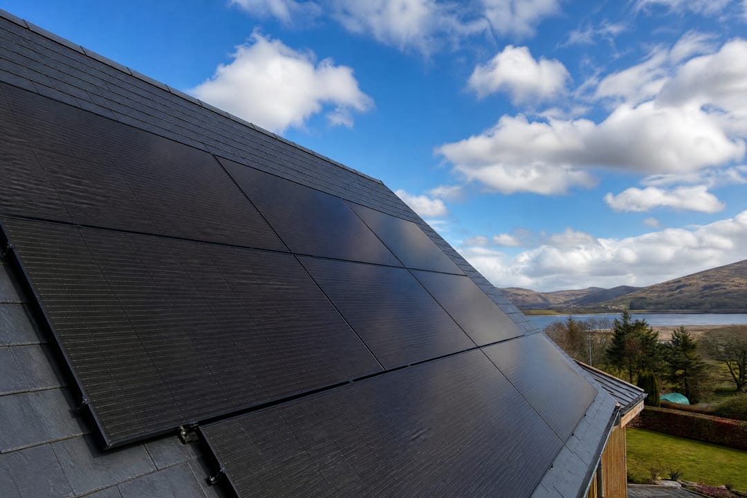 Black solar panels on a pitched roof under a blue sky