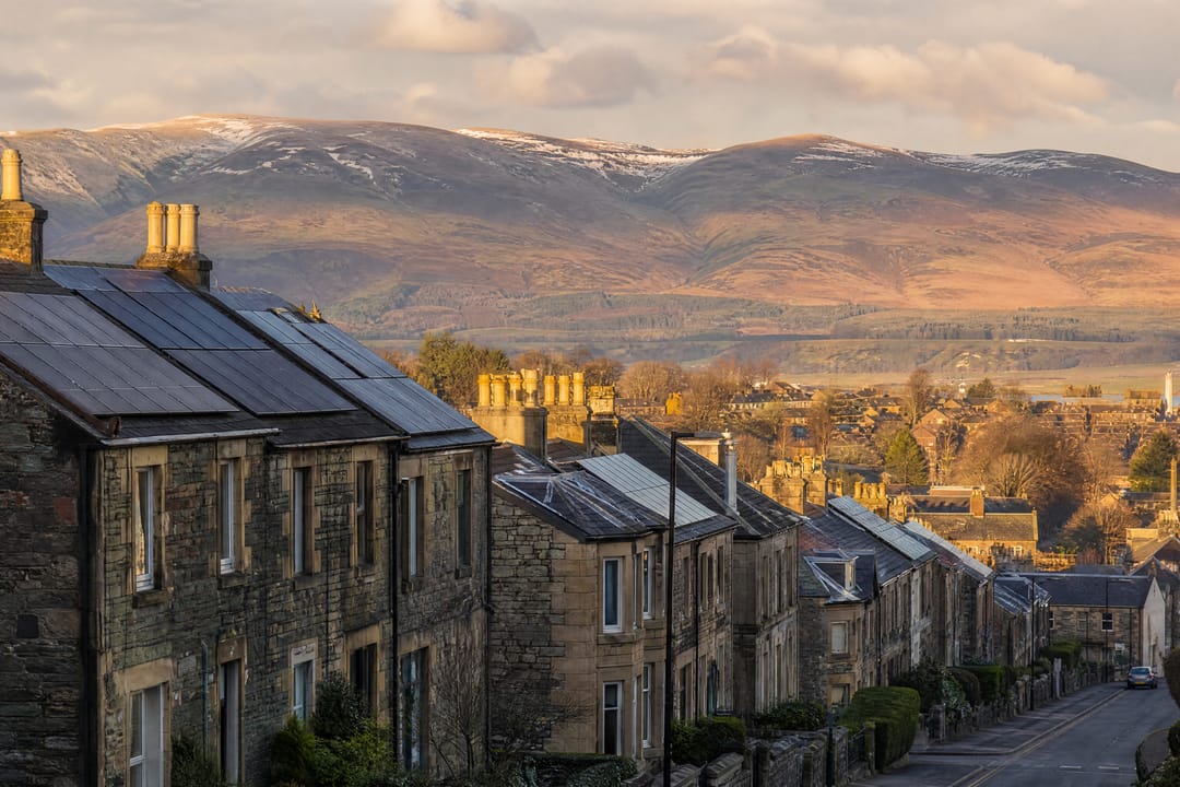 Stone terraced houses with solar panels below green hills